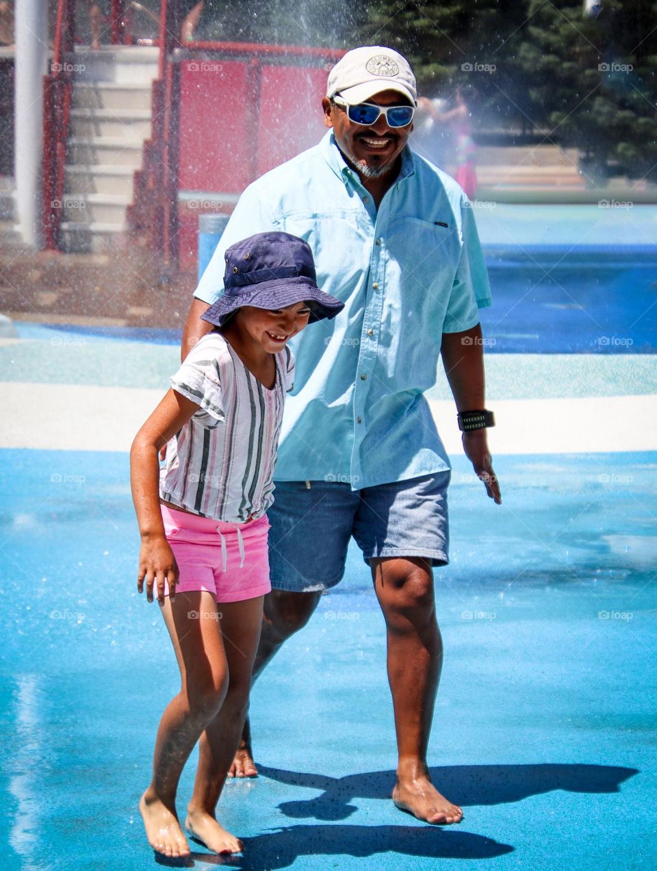 Father and daughter are on a splash pad during a hot summer day