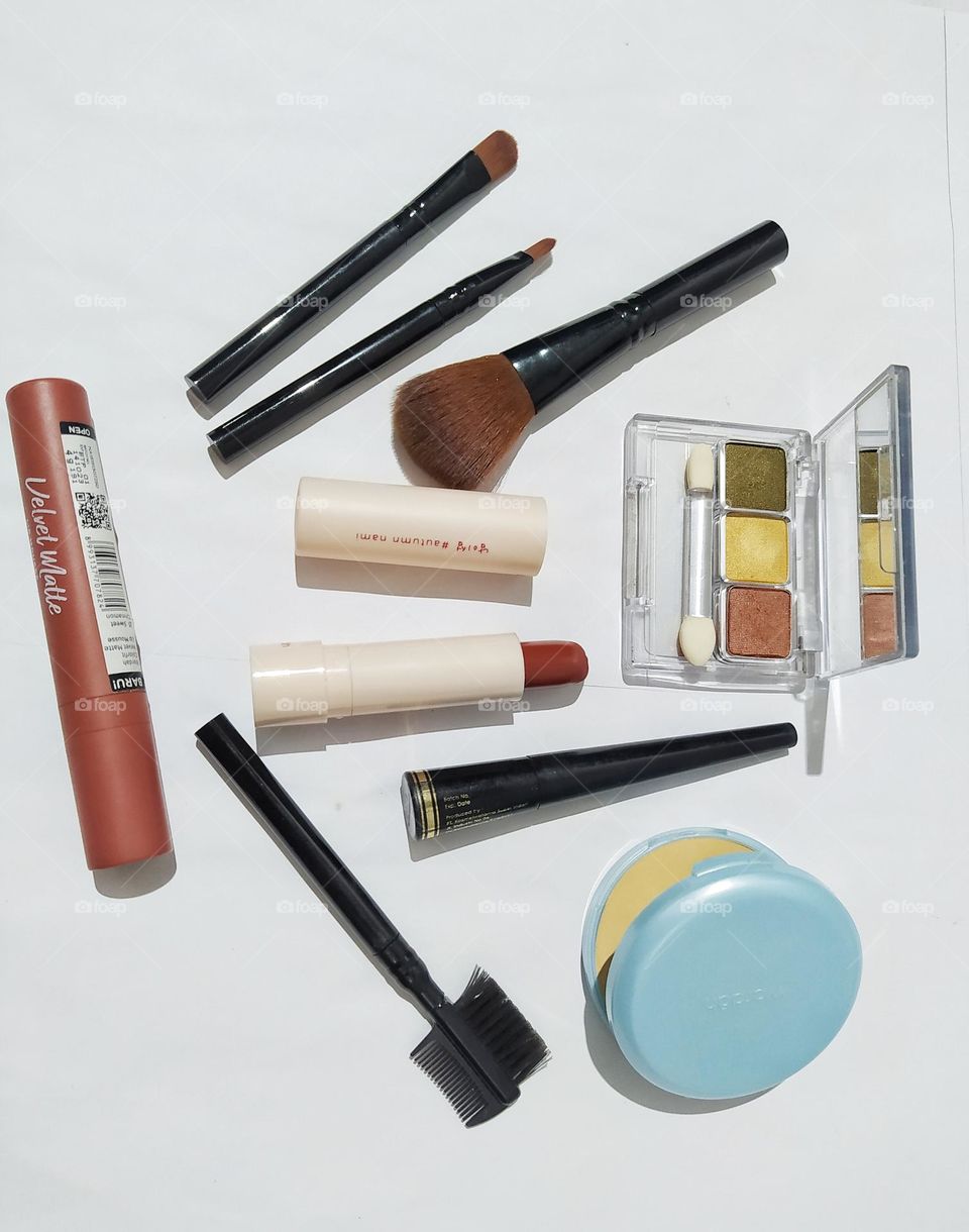 Top view, isolated on white background with some lipstick, powder, makeup brushes, eyeliner and eyeshadow kit