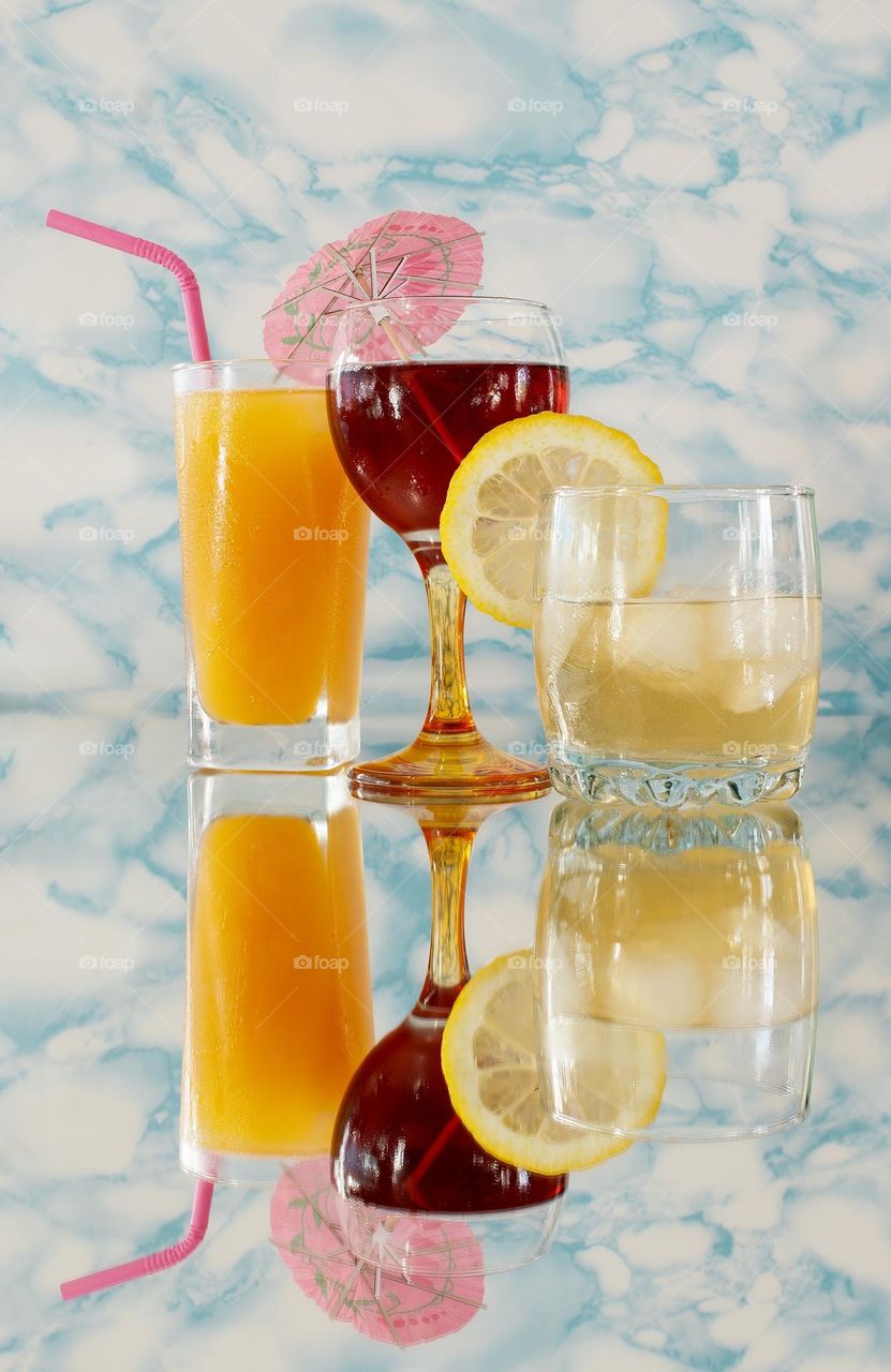Summer drinks and cocktails on a reflective surface against a marbled pattern background 