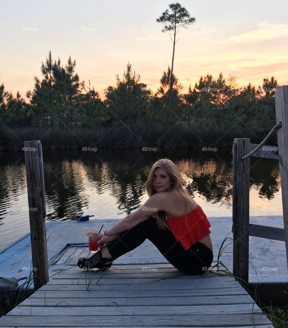 Blonde girl sitting by the water at sunset