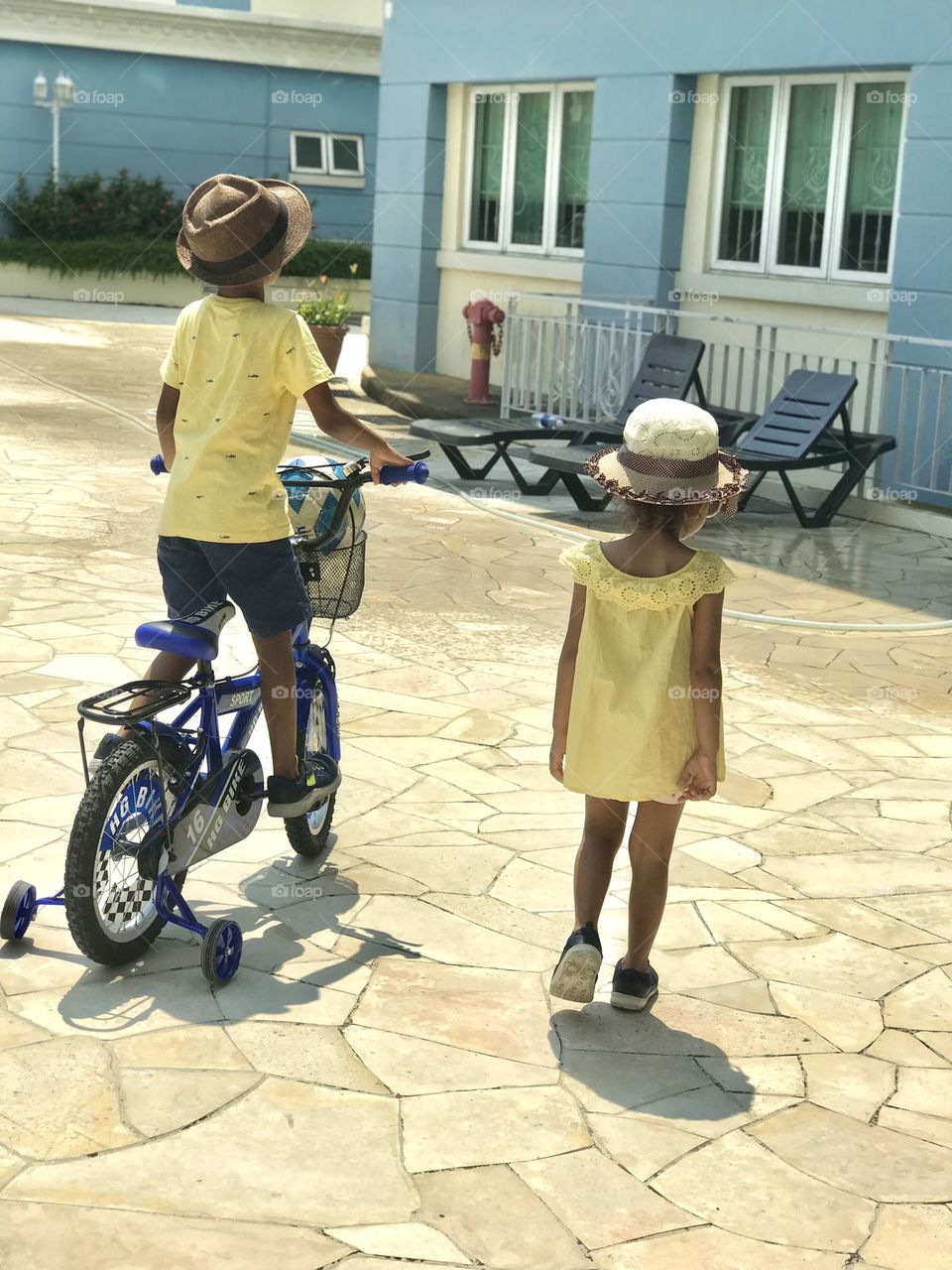 Kids wearing yellow summer outfits and hats on their head and going towards the swimming pool.