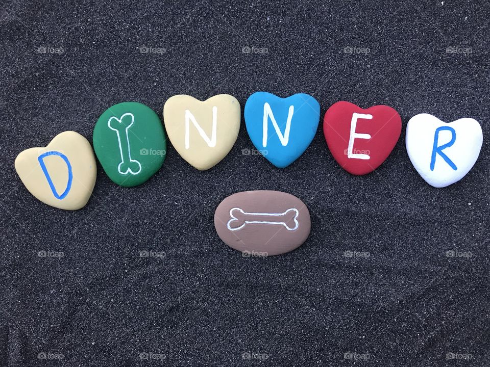 Dinner word with multicolored stone hearts over black volcanic sand 