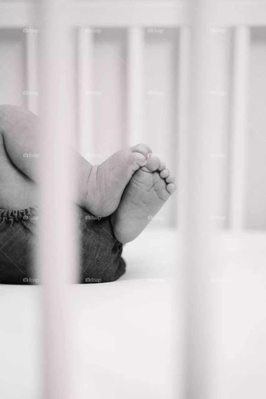 Stunning close up of a newborn’s feet and toes in black and white. The background and foreground of the baby crib are blurred, allowing for emotions to take over such a special time of life.