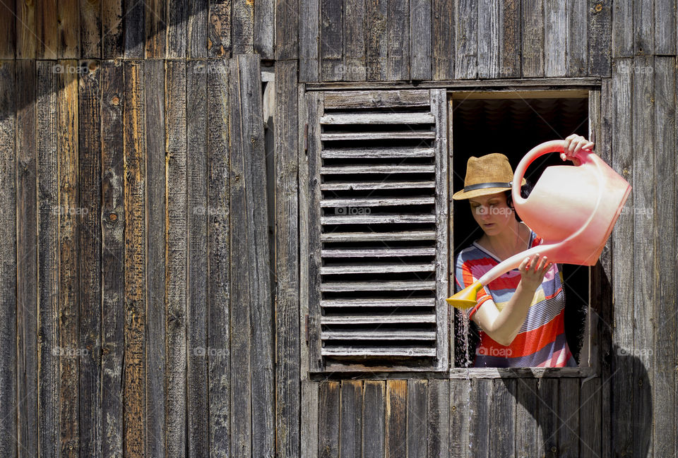 A woman on the wooden window holds pink watering can