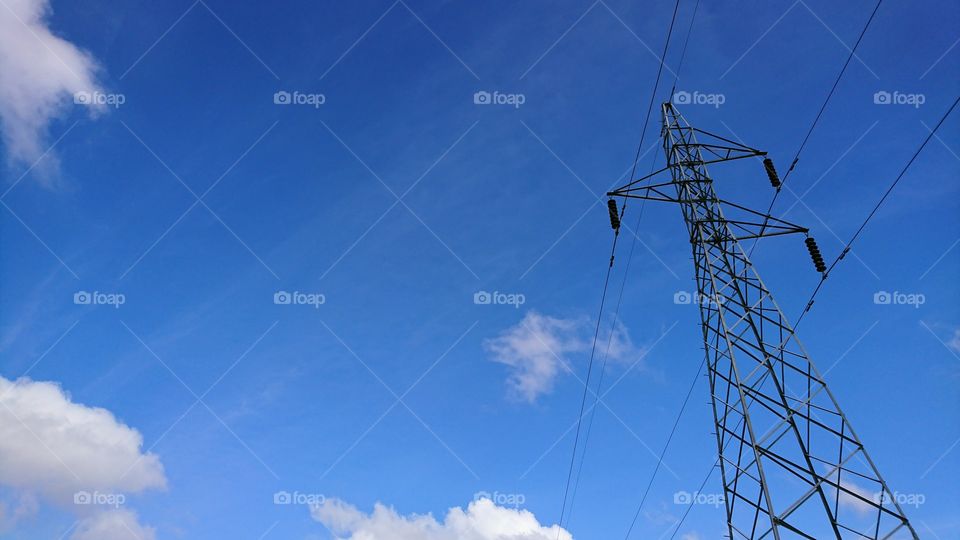 High voltage tower with power line on bright sky background