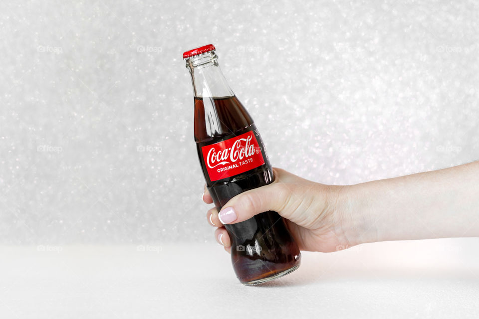 Female hand holding Coca-cola glass bottle on white glitter background