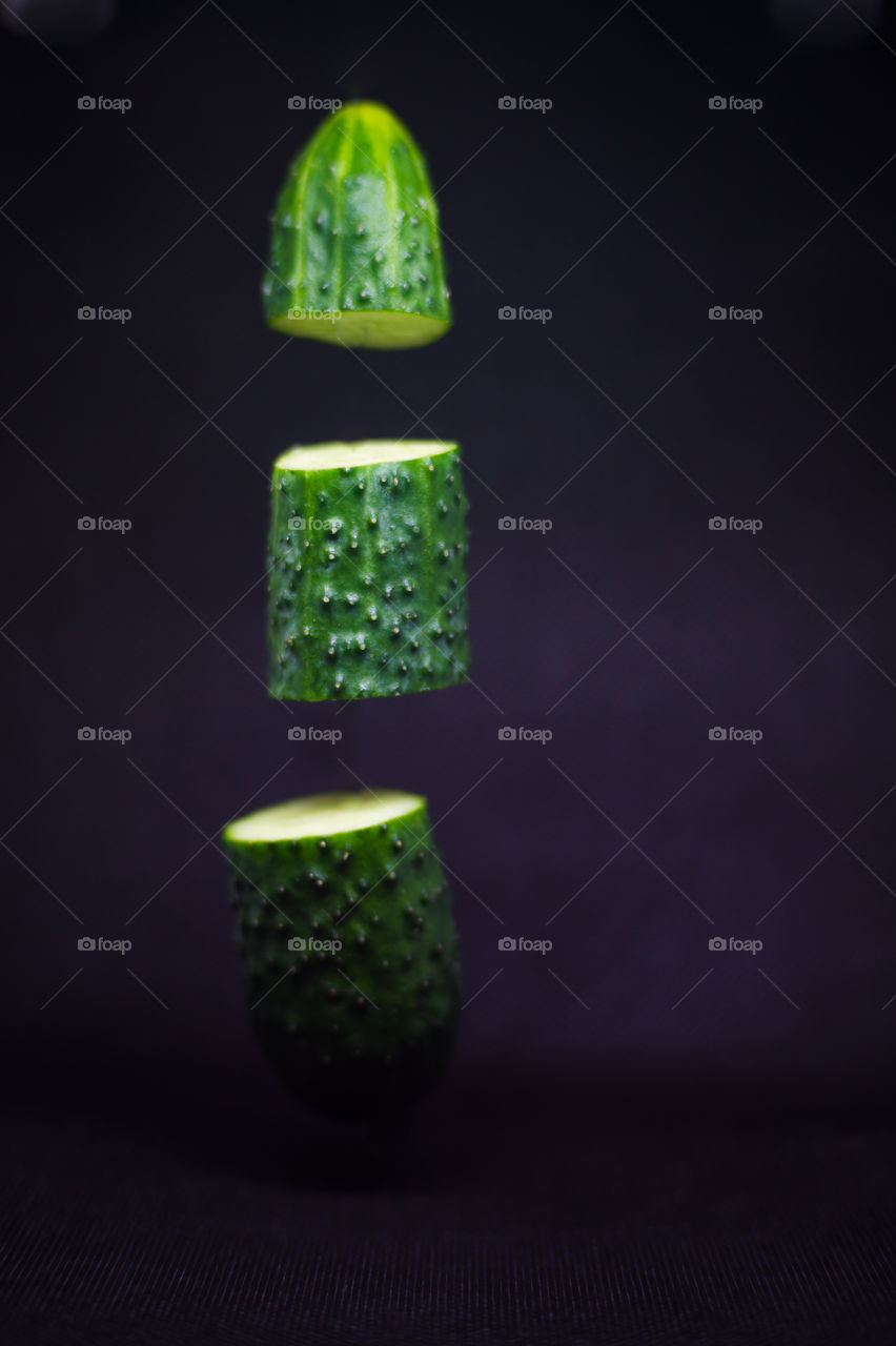 Close-up of a cucumber cut into three parts in the air on a black background.
