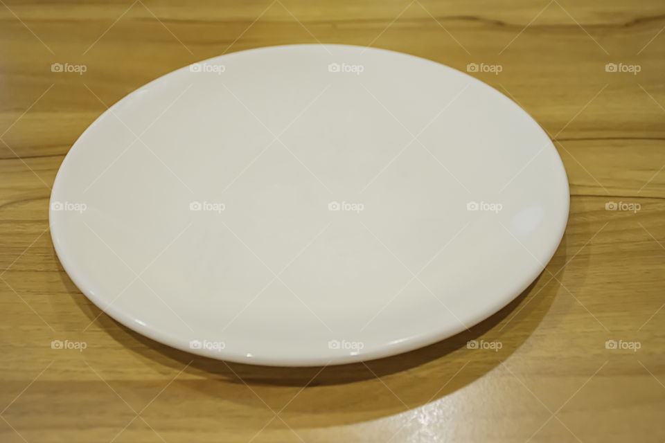 Top view of the white ceramic plate on a wooden table