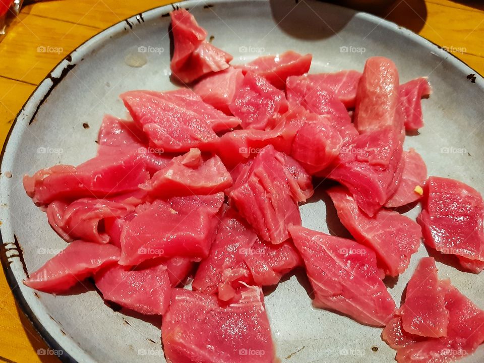 The red meat that has been cut into small pieces and they are put on a metal blue plate.