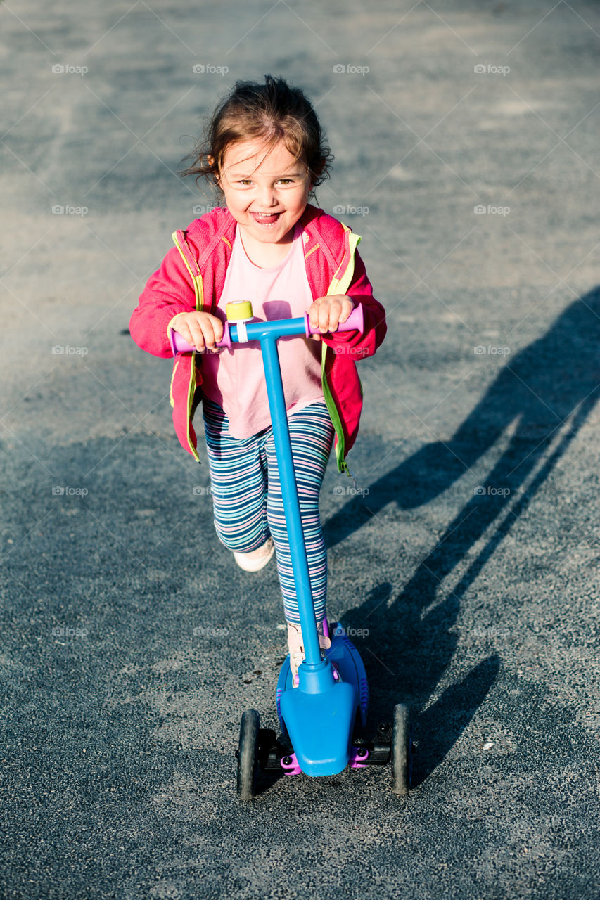 Little adorable girl having fun riding on scooter, playing outdoors. Real people, authentic situations