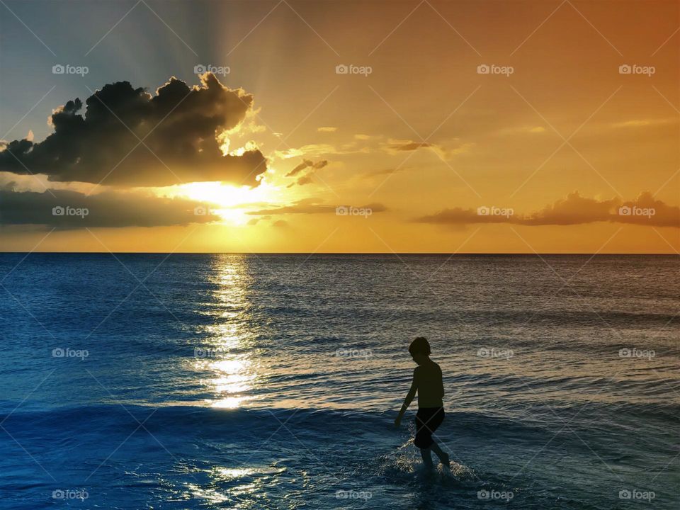 Small boy in the ocean during a vibrant golden sunset.