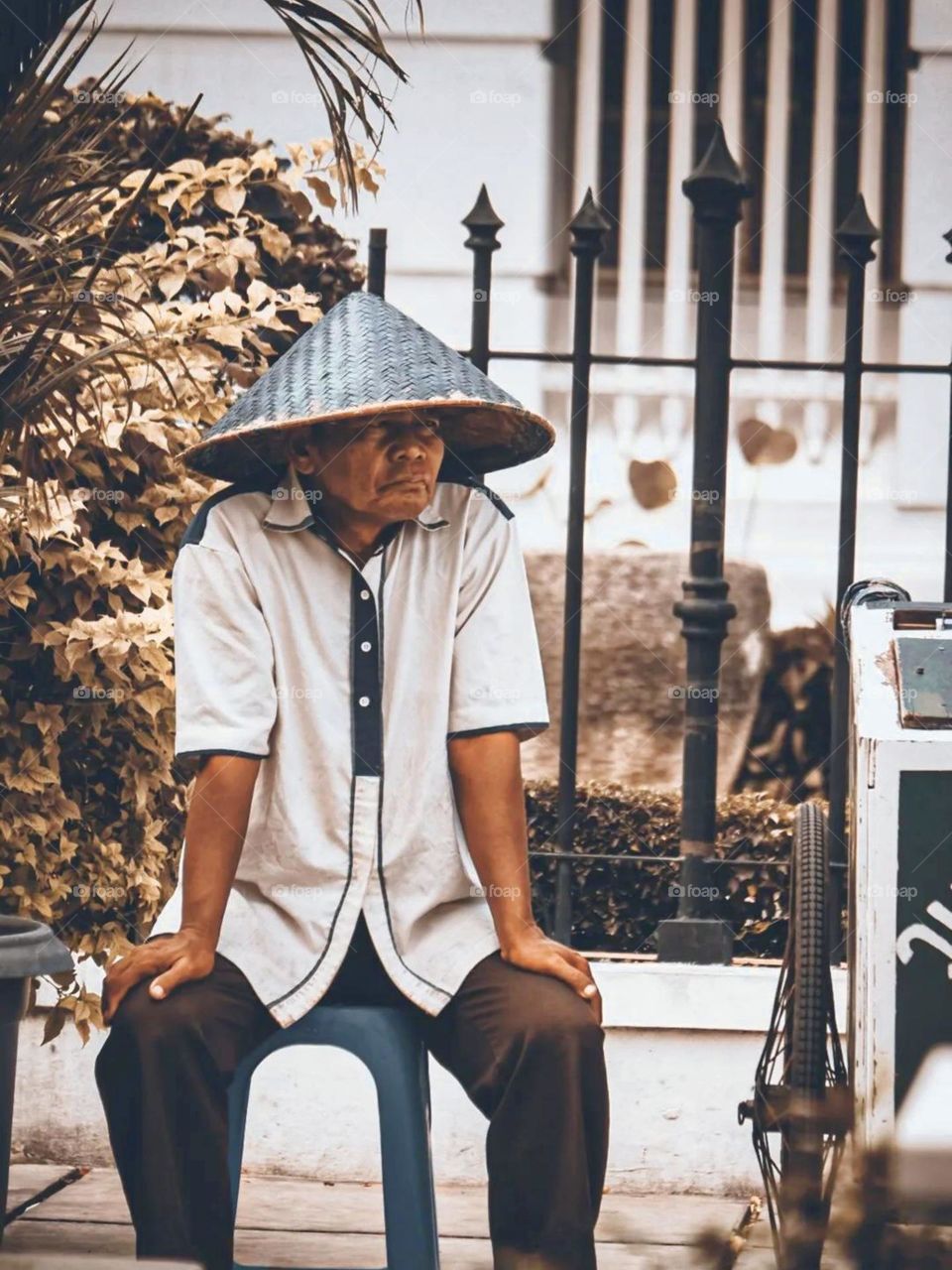 Close-up of a person wearing a straw hat, sitting outdoors. A person sits on a plastic chair, with a relaxed body position