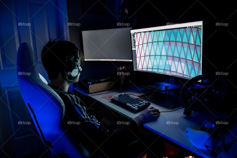 Teenage boy wearing headphones and sitting at a gaming computer in his bedroom 
