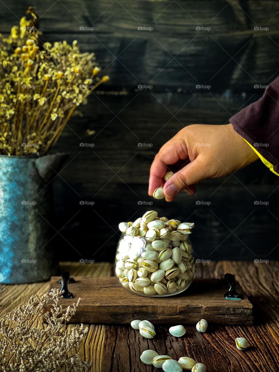 Pistachio nuts good for health. A hand holding a pistachio nut and some nuts in a clear glass jar