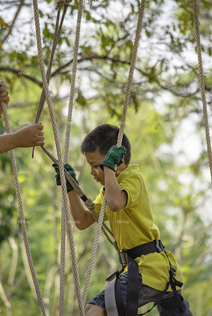 Asean boy nodes the rope and smiling happily in camp adventure Background blurry tree.