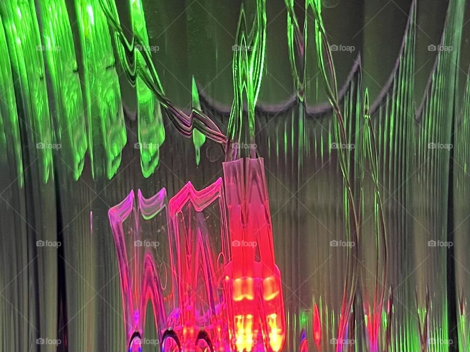 Abstract pink and green lights shining through a beveled glass vase.