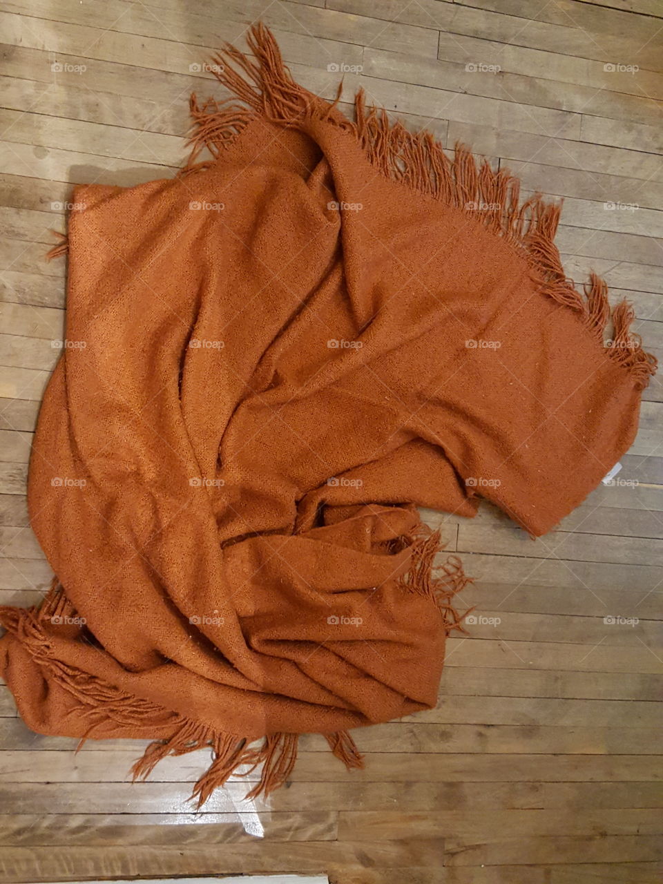 Orange blanket dropped casually onto hardwood floor.