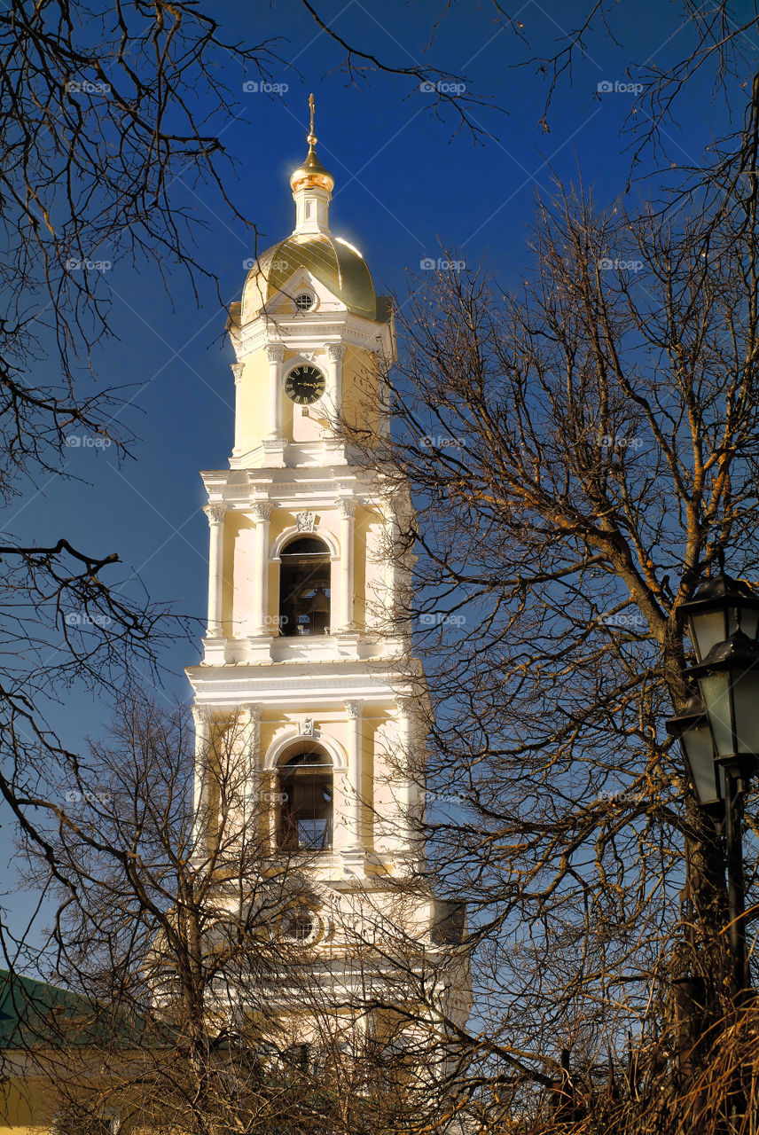 View of the bell tower of Holy Trinity Seraphim-Diveevsky monastery (Russia, Diveevo) through the branches of unblown trees against the background of the blue sky on a sunny spring day