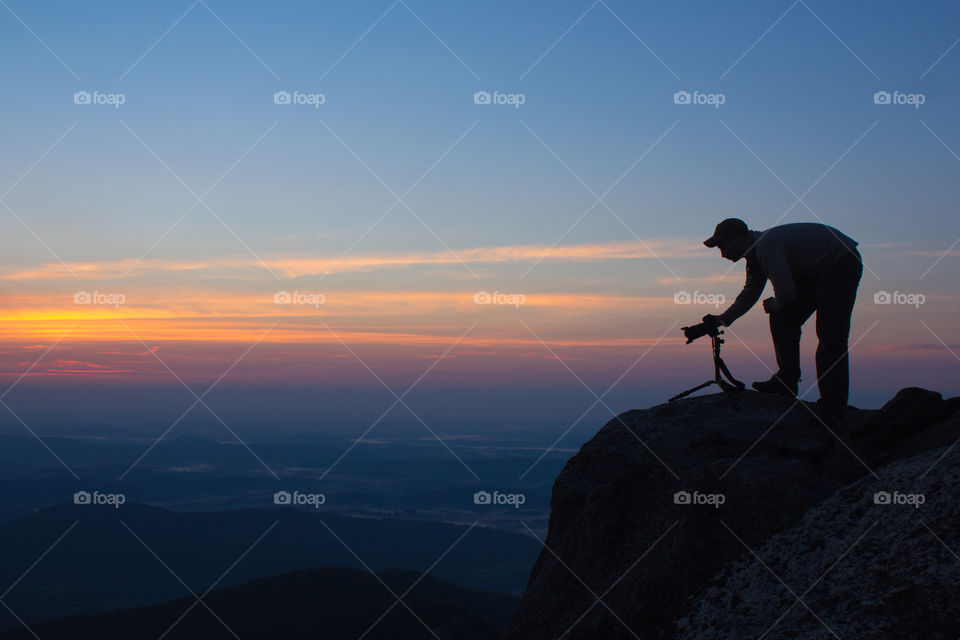 Silhouette of a photographer with camera on top of mountain
