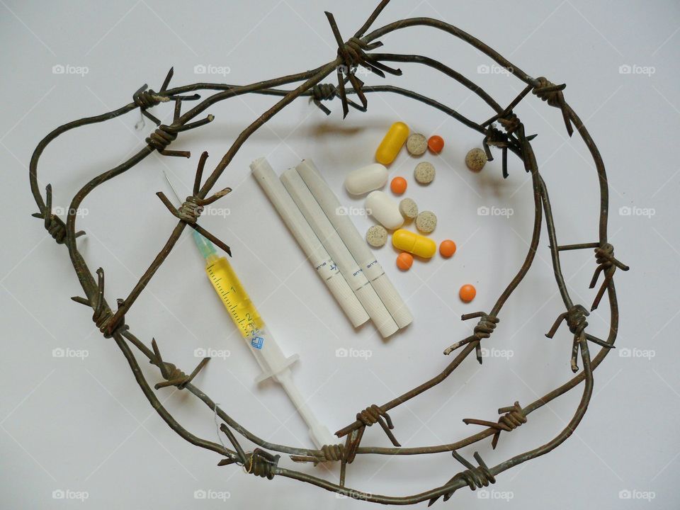 syringe, tablets, cigarettes surrounded by the barbed wire on a white background