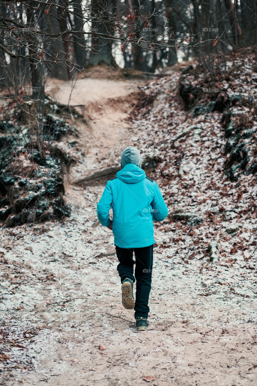 Young man running outdoors during workout in a forest among leafless trees on cold freeze winter day. Boy is wearing sport clothes