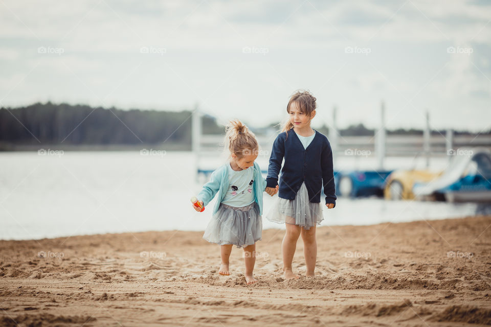 Little sisters on lake coast at sunny evening. 