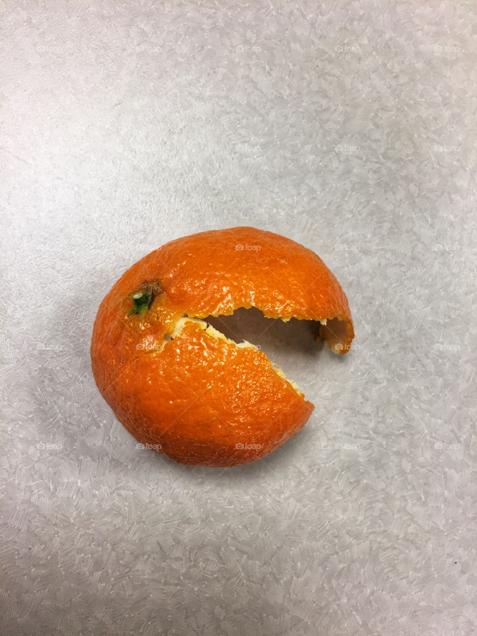 An orange peel sits discarded on a grey tabletop. This fruit rind looks a little like Pac Man