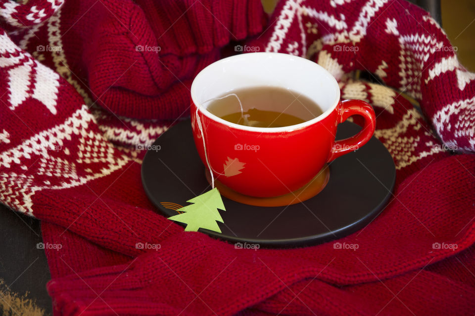 a red cup of tea stands on a chair wrapped in a warm red Christmas sweater, tea label in the form of a green Christmas tree