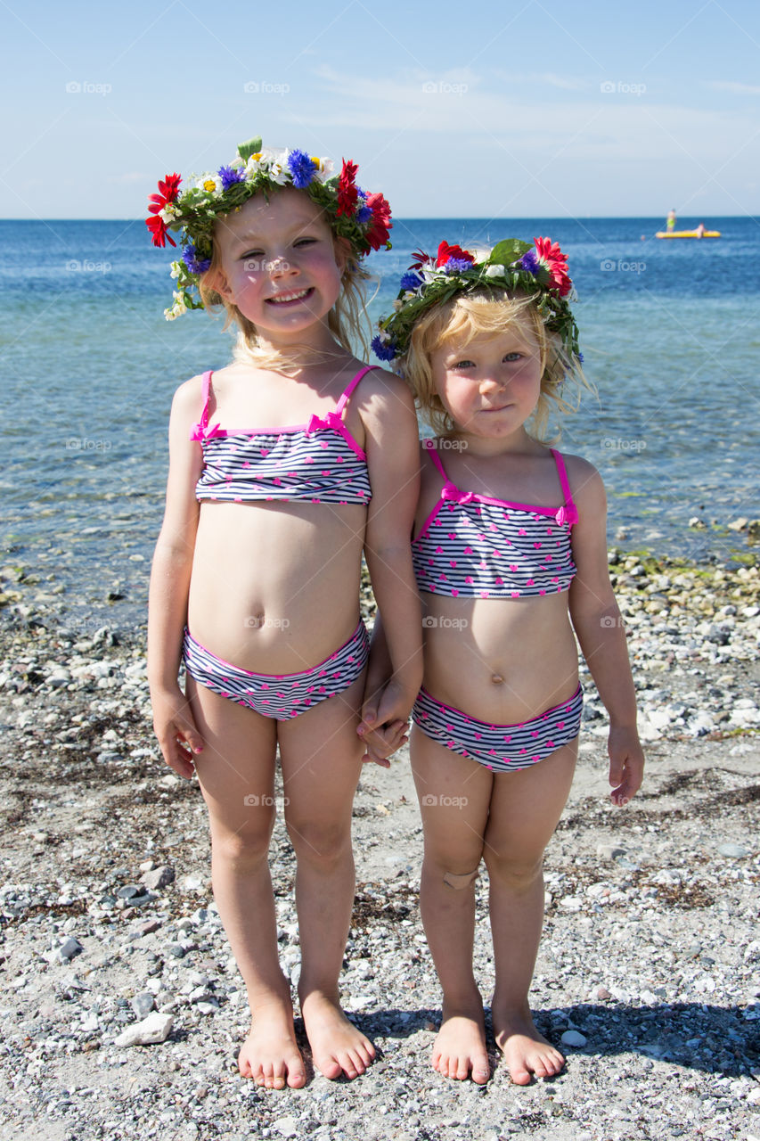 Cute little sisters standing at beach wearing wreath