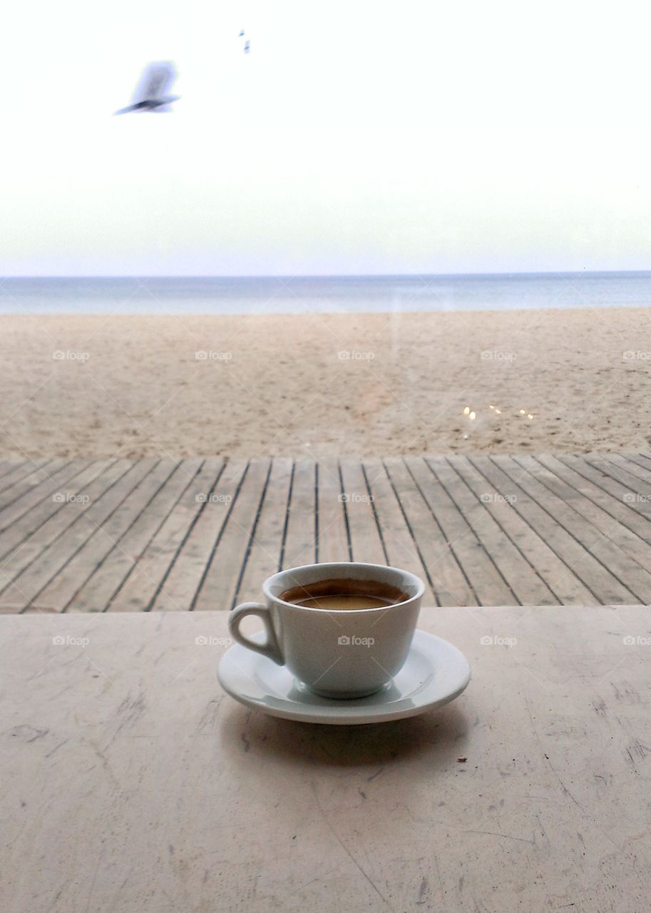 White coffee cup on wooden table with sand beach background