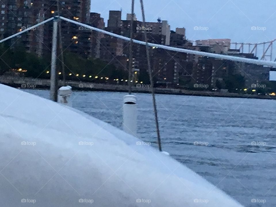 A seaside scene in the twilight of upcoming nighttime featuring the white front deck of our sailboat „Salvation“, the silvery waters of the East River and the skyline of Manhattan’s Upper East Side. 2017. Hypnotic Productions 