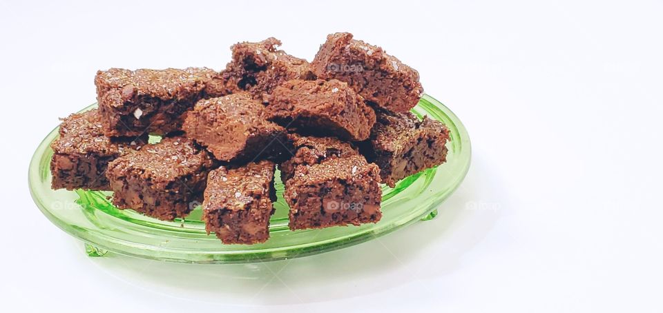 Chocolate brownies on a green glass plate with a white background 
