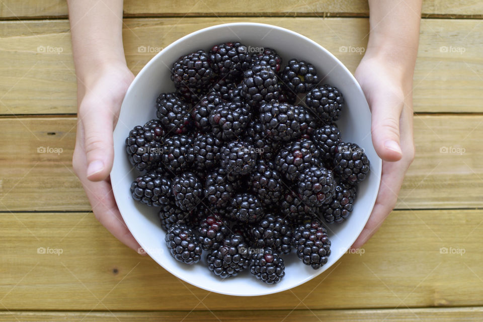 Hands holding a bowl of blackberries