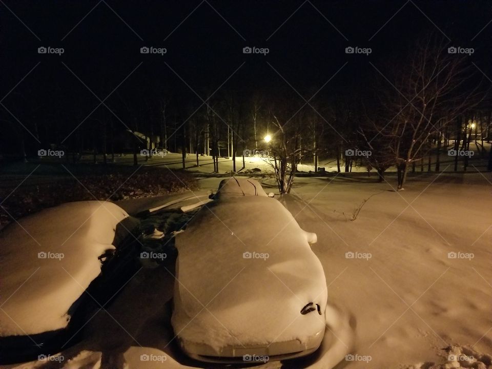 Snow Covered cars lit up by security lights.