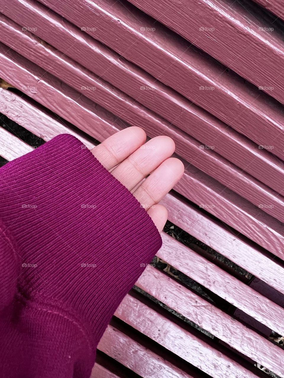 A person’s hand wearing a magenta sweatshirt against mauve background. 