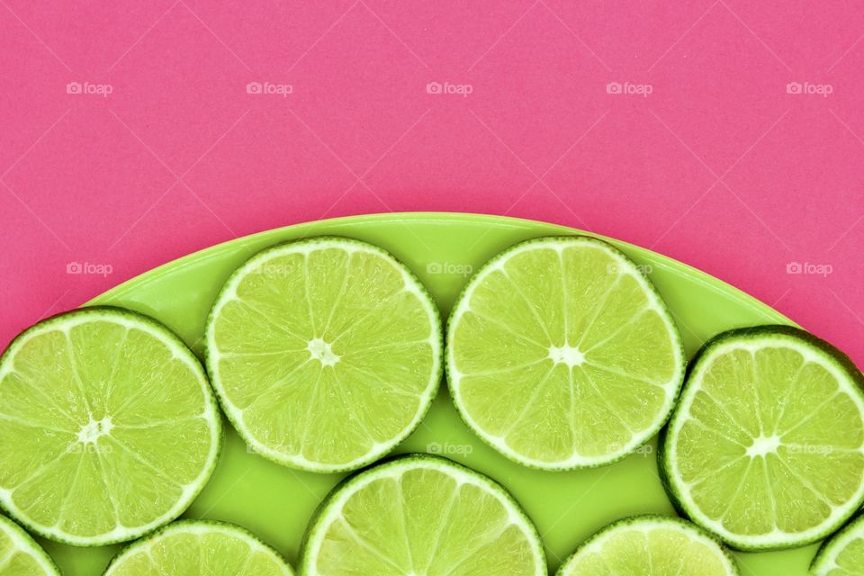 Color Love - minimalistic flat lay of lime slices on a green plate against a bright pink background