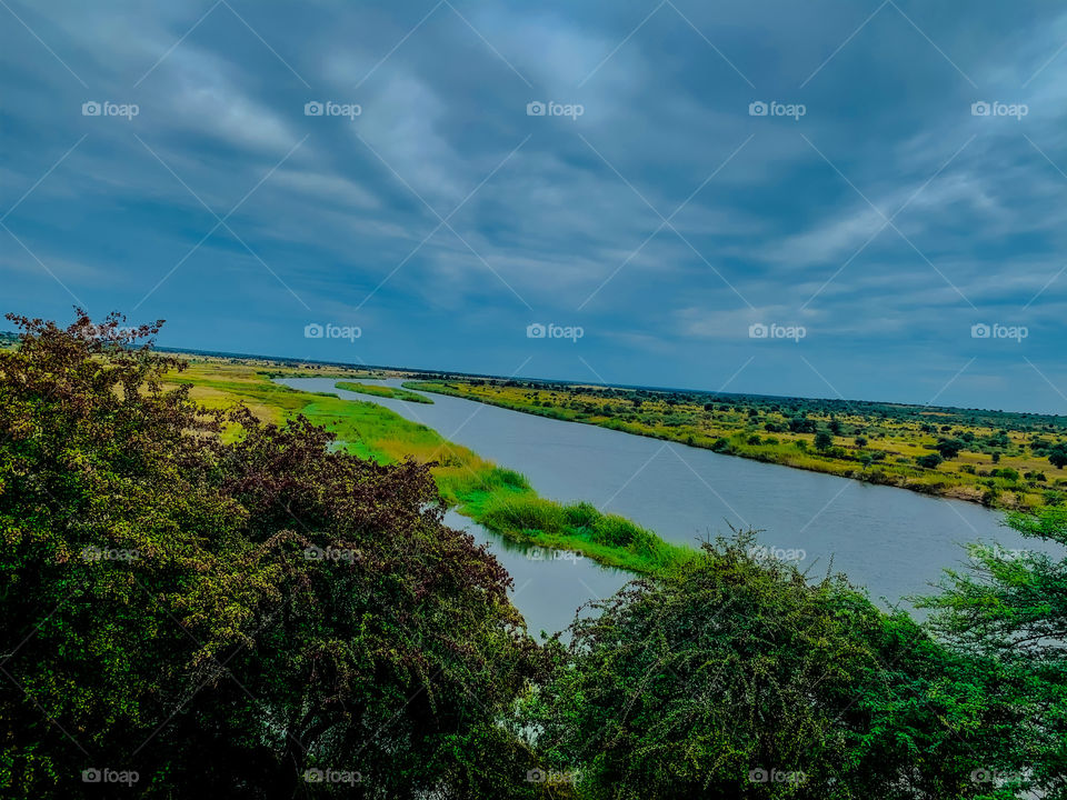 A beautiful view of the Kavango river from up, green, brown grass and scattered trees. Full water levels and an overcast sky. 