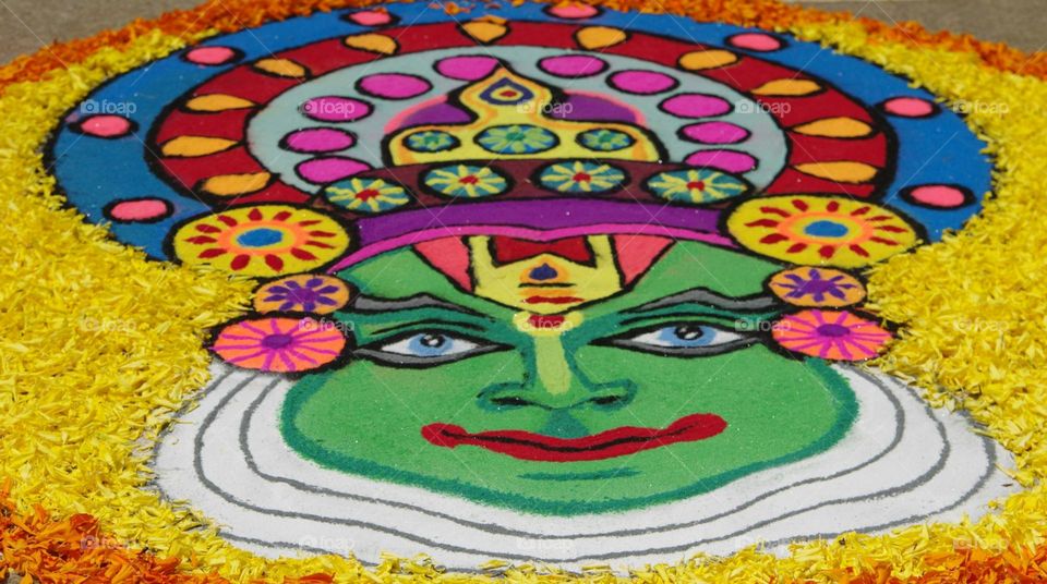 a decorated cake with a face on it

the face of a kathakali dancer portrayed on the ground using flower petals and colored rice flour during Onam festival celebrations.