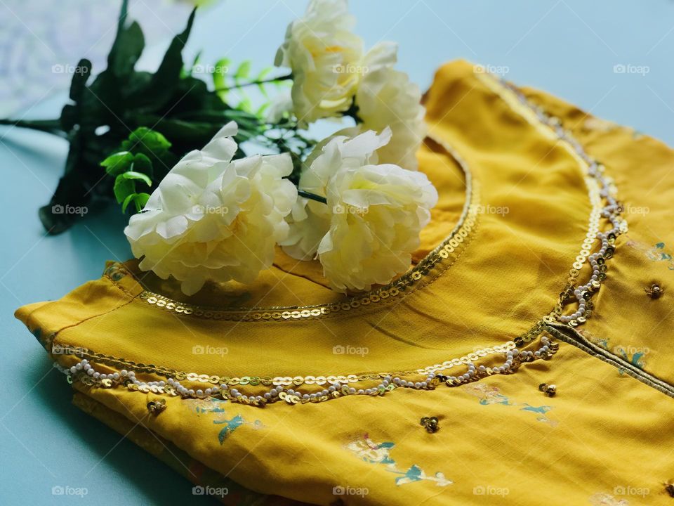 Beautiful yellow dress with detailed embroidery work under the neck and white and yellow mixed bunch of flowers near the dress 