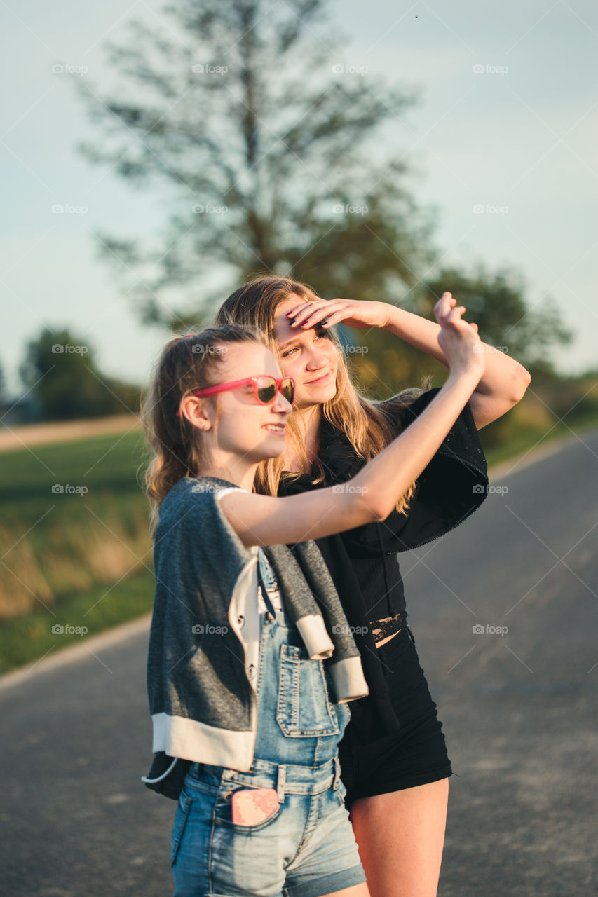 Teenage smiling happy girls having fun walking outdoors, hanging, spending time together on summer day. Real people, authentic situations