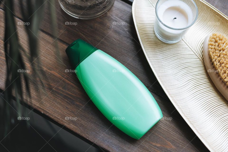 Bottle of shampoo, aromatic candle in glass and wooden brush with natural bristles on metal tray on the wooden window sill, mockup