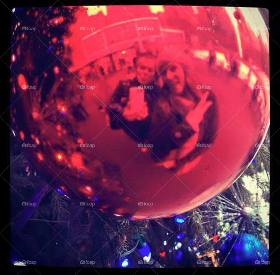 Reflection of friendship. Two friends in New York City sneak a selfie in the reflection of a giant Christmas ornament at Rockefeller Plaza