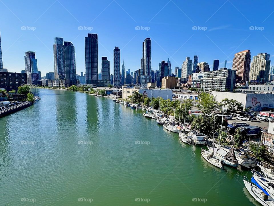 From the “Pulaski Bridge” that connects “Greenpoint”, Bklyn to LIC, Queens we look upon “Newtown Creek”, ocean inlet of the “East River” with all its boats. In the distance we see “Manhattan” incl. the “Empire State Bldg”. 2024. Hypnotic Productions