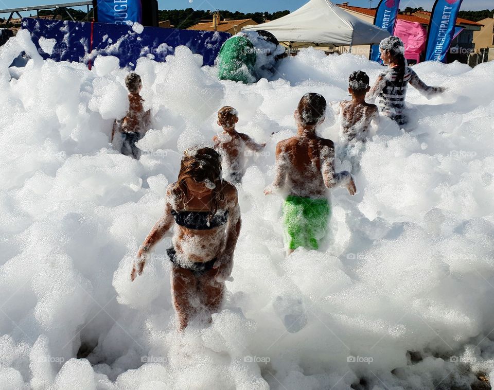 6 Children covered in foam at foam party on the beach