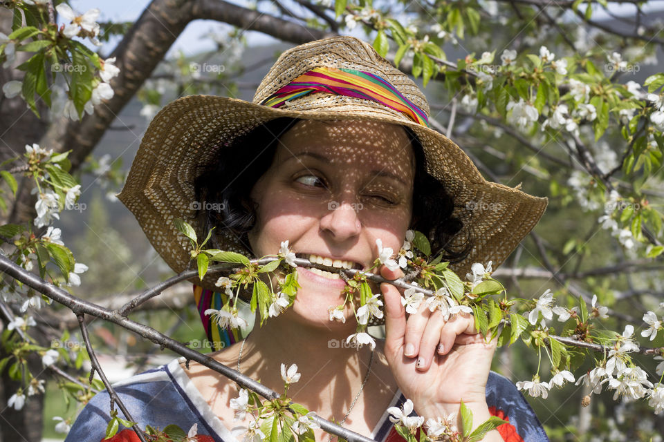 Funny portrait of a woman with straw hat biting spring tree branch