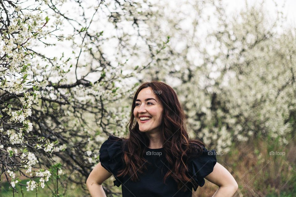 Young millennial woman smiling and being happy while surrounded by flowering tress.