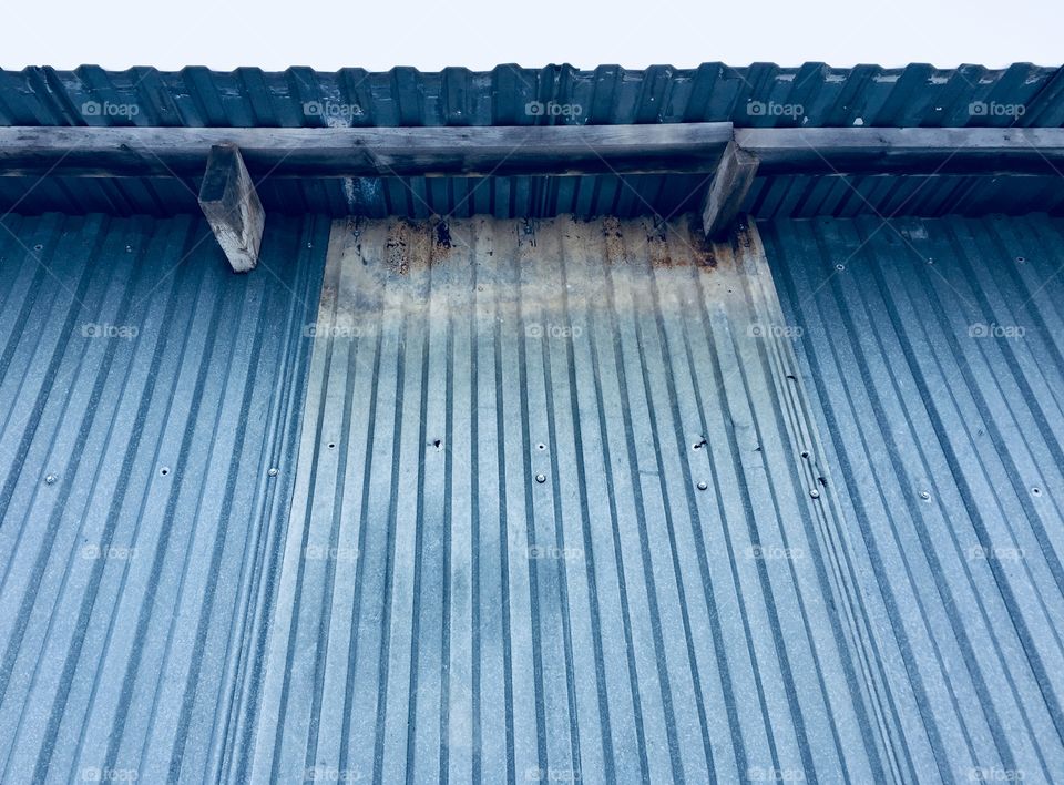 Wooden rafters and overhang of a metal building against a pale blue sky