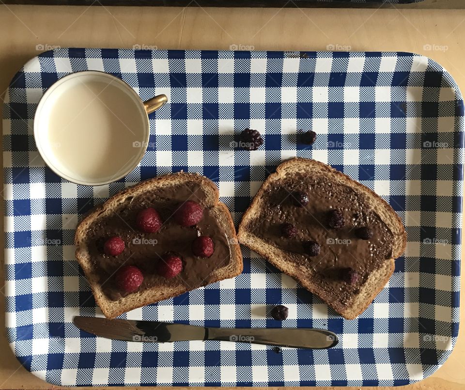 Delicious lunch of a chocolate Nutella sandwich with raspberries and blackberries with a tea cup and knife to spread displayed on a blue and white serving tray. USA, America 