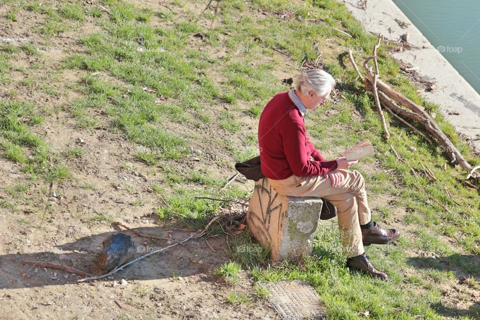 old man reading in the river bank