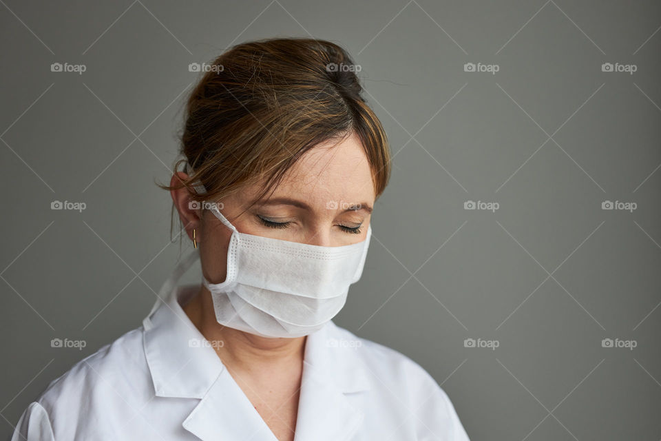 Doctor with face covered with mask. Portrait of young woman wearing the uniform, cap and mask to avoid virus infection and to prevent the spread of disease. Real people, authentic situations